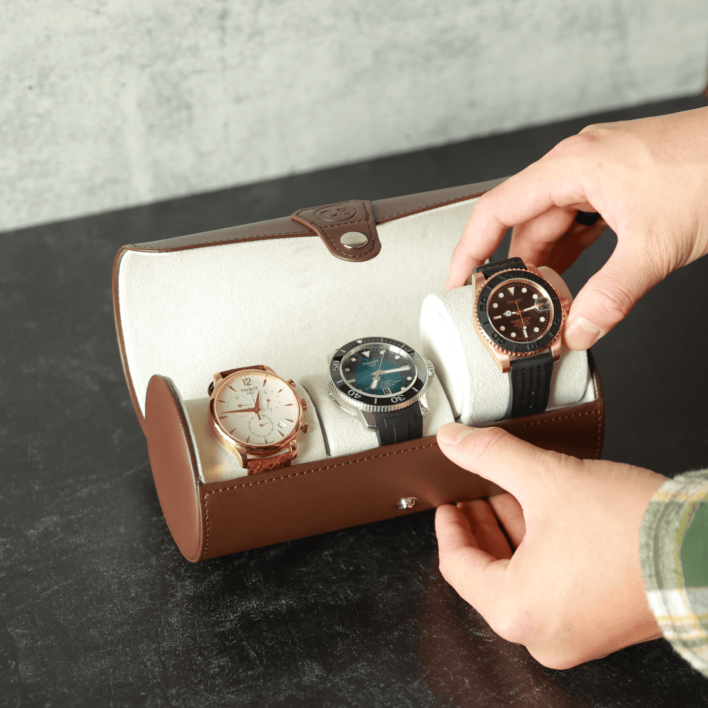 Person holding a vegan leather travel watch case with three watches inside, on a dark surface.